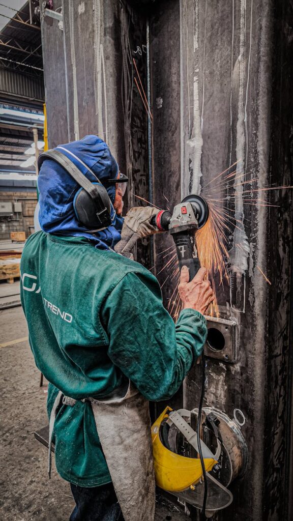 Worker in protective gear grinding metal with sparks flying in an industrial setting in Brazil.