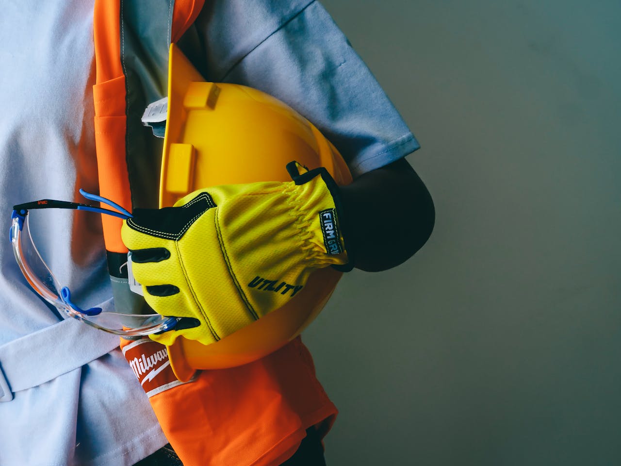 Close-up of a construction worker holding a hardhat and wearing PPE, including gloves and goggles.